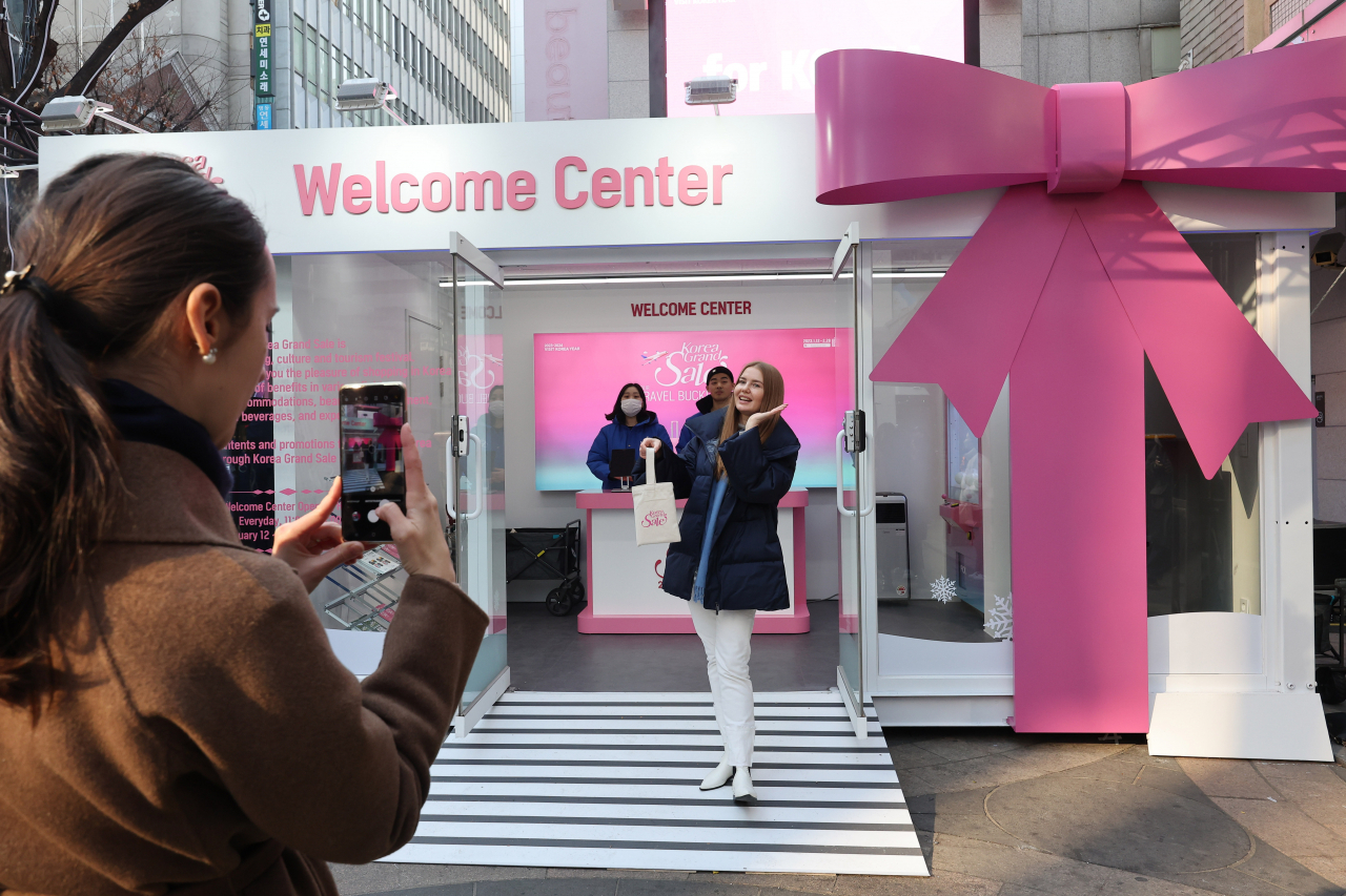 A tourist poses for a photo on Thursday in Myeong-dong, Seoul, outside one of the information booths for the Korea Grand Sale 2023. (Yonhap)