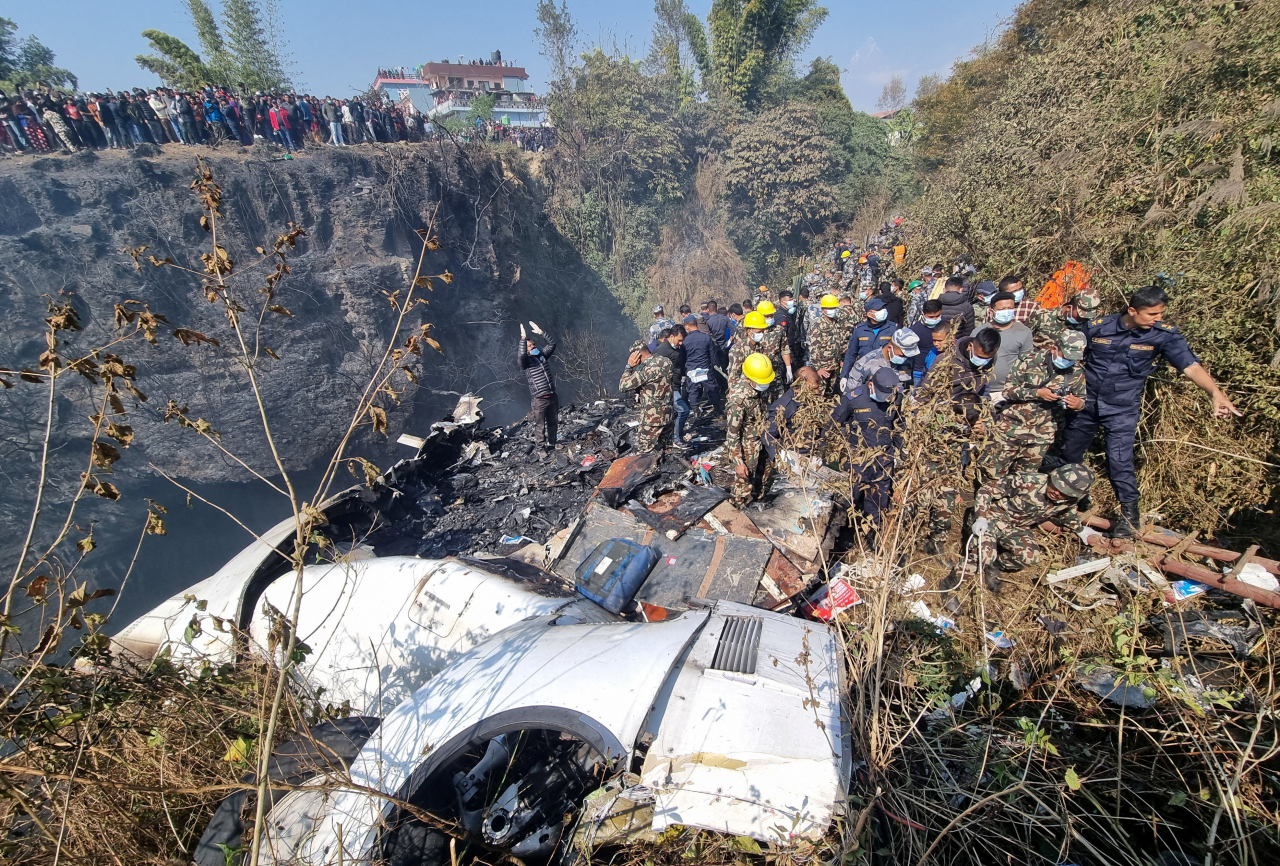 In this photo provided by a third party, rescue teams work to retrieve bodies at the crash site of an aircraft carrying 72 people in Pokhara in western Nepal on Sunday. (Reuters-Yonhap)
