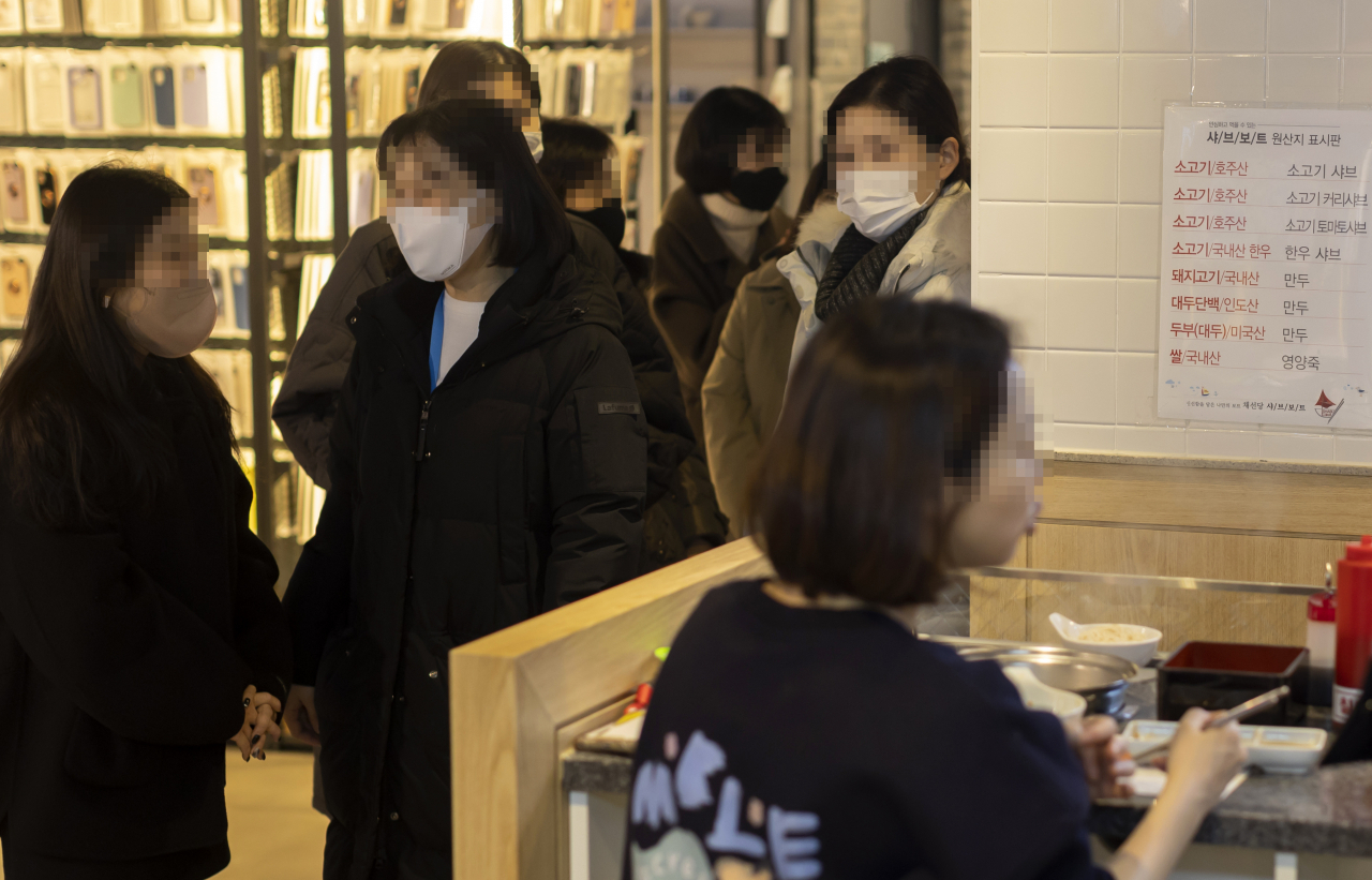 People wearing masks wait in line inside a restaurant in Seoul during lunch hour on Tuesday. (Yonhap)