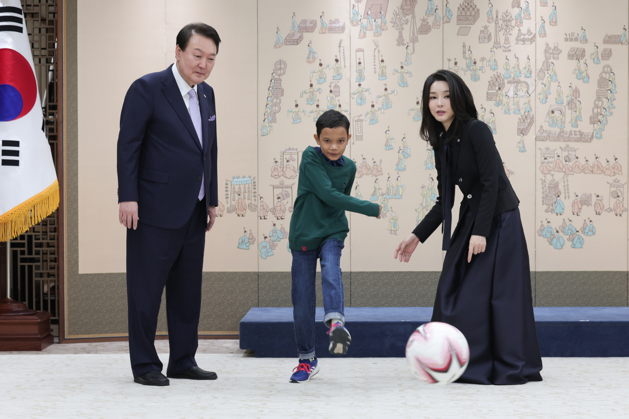 President Yoon Suk Yeol and first lady Kim Keon Hee watch 14-year-old Aok Rotha from Cambodia kicking a soccer ball at the presidential office in Yongsan-gu, Seoul, Tuesday. Rotha, who had heart surgery at the Asan Medical Center in Seoul after the first lady's visit to his home in Cambodia, was given the ball as a gift as he had never played soccer before, officials said. (Yonhap)