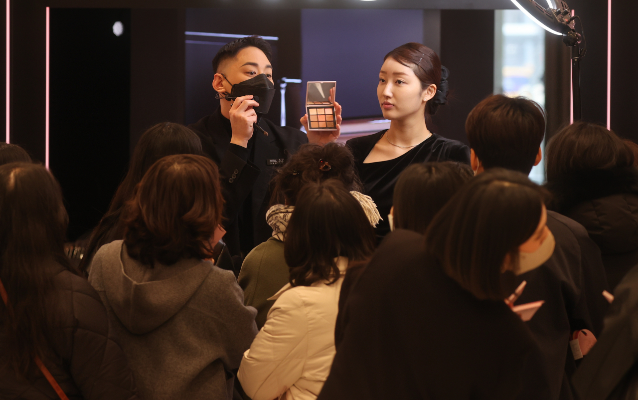 People watch a makeup demonstration at a department store in Seoul on Wednesday, after the government lifted an indoor mask mandate earlier in the week. (Yonhap)