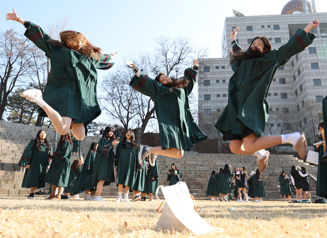 Students jump with joy, without wearing masks, to take graduation photos at a ceremony in Seoul last Wednesday. (Yonhap)