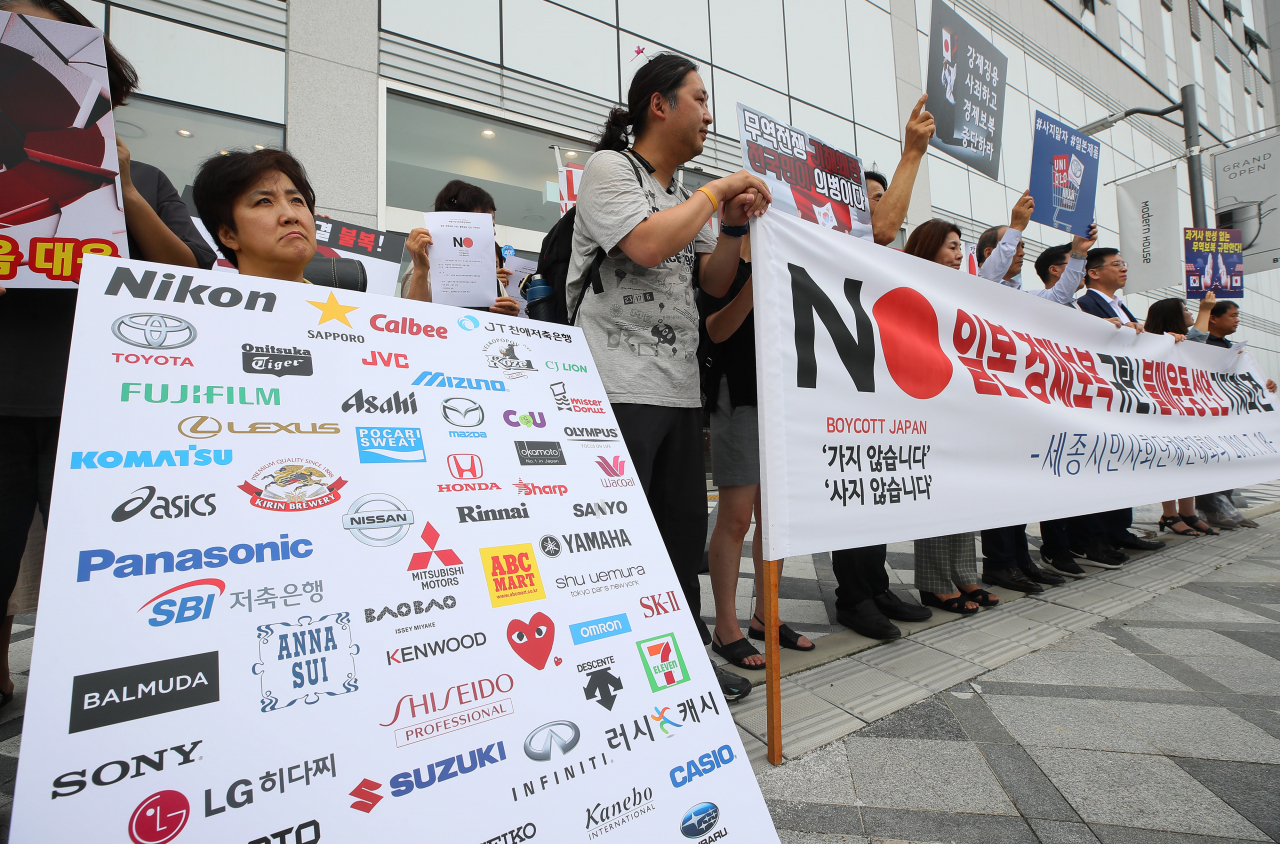 A civic group member holds up a sign with a collage of Japanese brand logos, urging people to join the 
