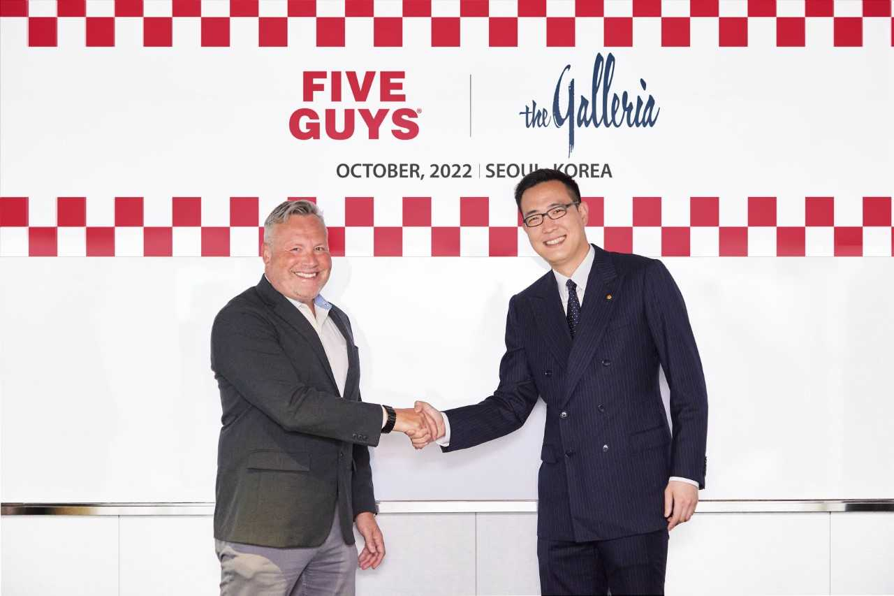 Will Peecher (left), senior vice president of operations at FGE International, the operator of Five Guys, and Kim Dong-seon, head of business strategy at Hanwha Galleria, pose for a photo after signing a business agreement at a Seoul in October 2022. (Hanwha Galleria)