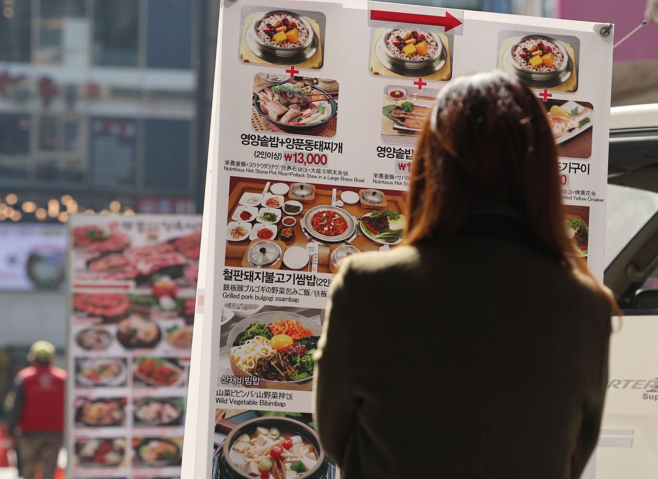 A woman looks at the price tag in front of a restaurant. (Yonhap)