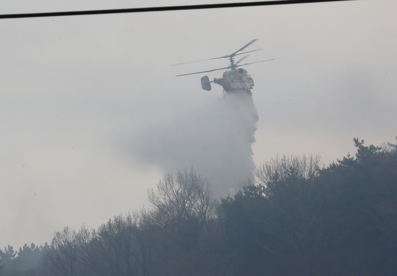 A chopper sprays water over a hill in Hongseong, South Chungcheong Province, on Tuesday, where a wildfire has continued for the third day. (Yonhap)