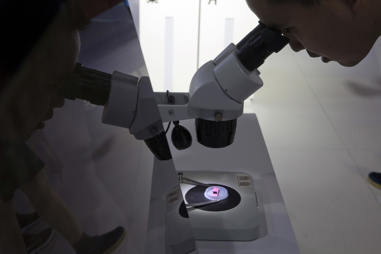 A visitor to the 21st China Beijing International High-tech Expo looks at a computer chip through the microscope displayed by the state-controlled Tsinghua Unigroup project which has emerged as a national champion for Beijing's semiconductor ambitions in Beijing, China on May 17, 2018. (AP-Yonhap)