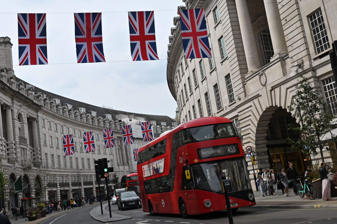 A red London bus passes beneath Union flags on Regent Street, in central London on Sunday ahead of the coronation ceremony of King Charles III. (AFP-Yonhap)