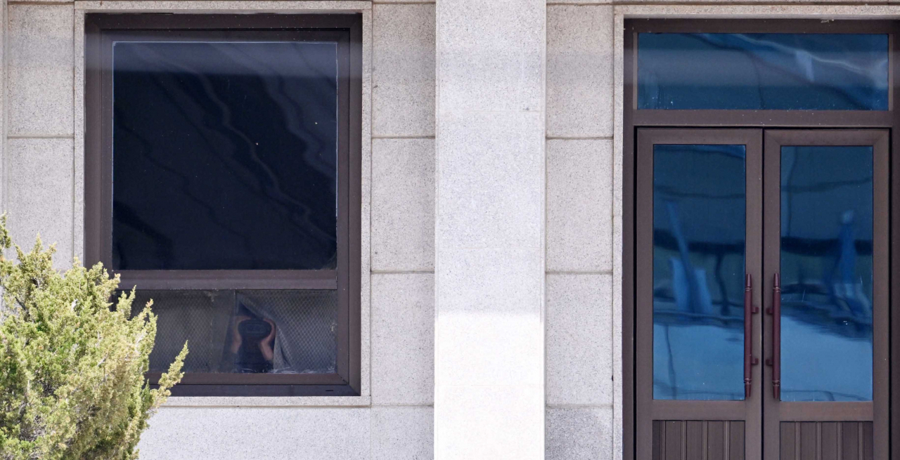 A North Korean soldier peers at Chief of Staff of the United States Army Gen. James McConville through a telescope from inside the Panmungak building on the north side of the Joint Security Area on Tuesday, slightly opening the curtains. (Lee Sang-sub/The Korea Herald)