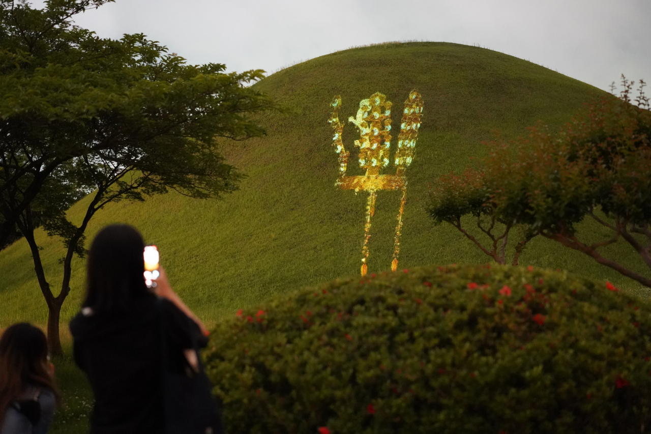 A tourist takes a photo of a projecion of a gold crown on the Hwangnam Daechon Tomb at Daereungwon in Gyeongju, North Gyeongsang Province, Tuesday. (Lee Si-jin/The Korea Herald)