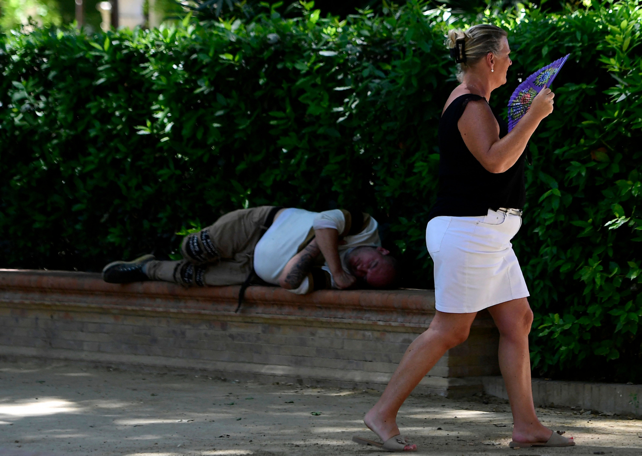 This file picture shows a woman using a fan to cool-off walks past a man lying in the shade in Seville in Spain on April 26, 2023. (AFP)