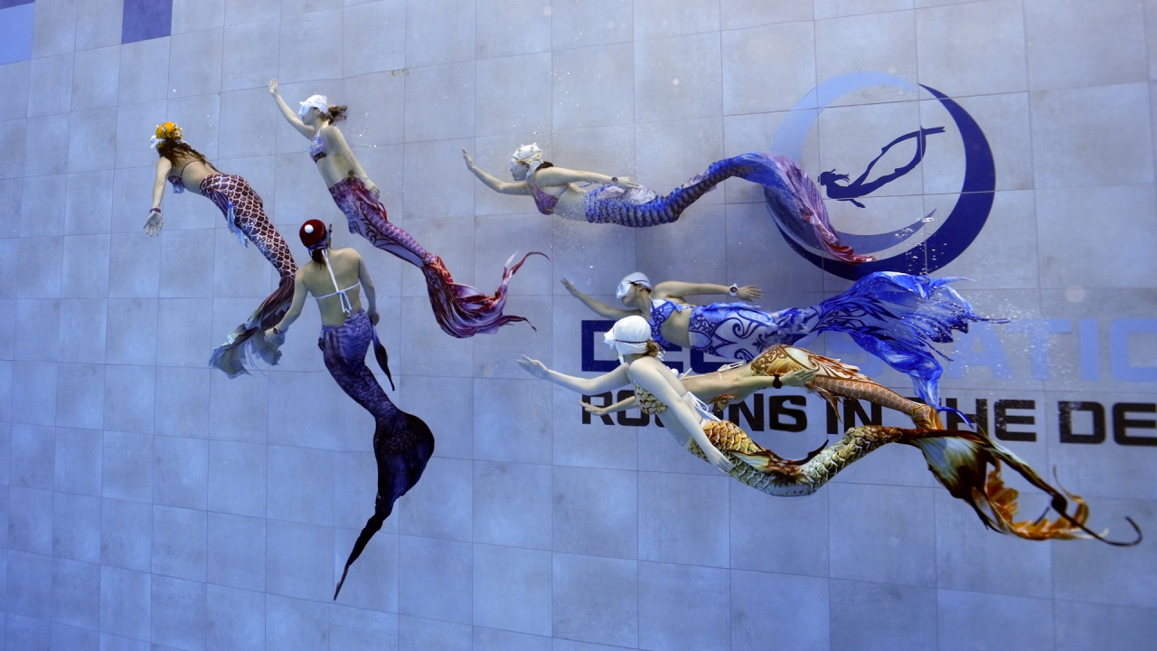 A group of mermaid practitioners swim underwater (Mer Freediving)