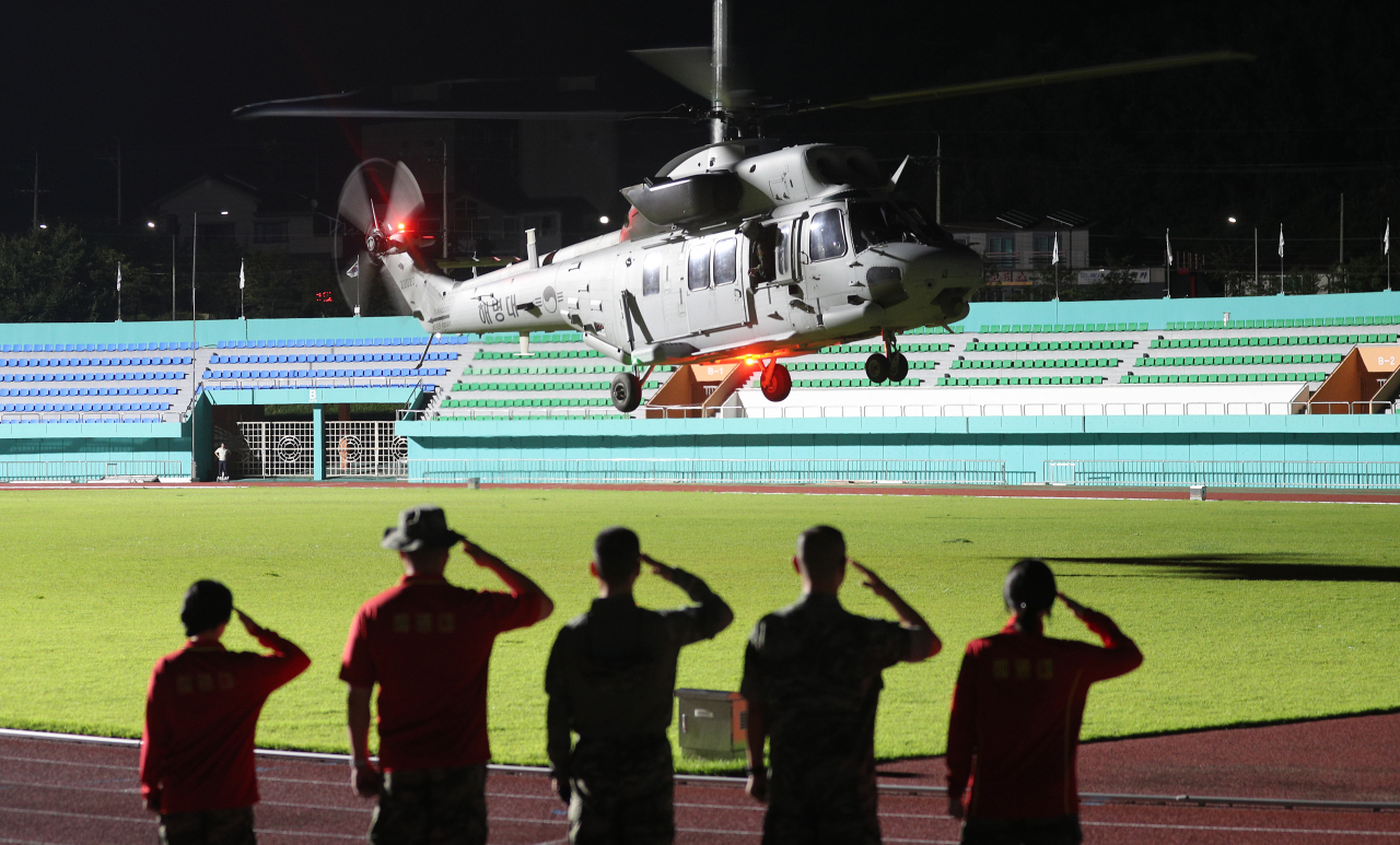 A helicopter carrying the body of Lance Cpl. Chae Su-geun, who was swept away by strong waters in Yecheon-gun, North Gyeongsang Province, is saluted by members of the Marine Corps at Yecheon Stadium on Thursday. (Yonhap)