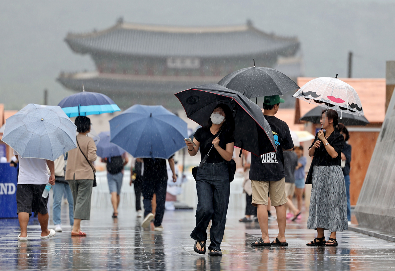 People holding umbrellas walk across a crosswalk in central Seoul on Sunday as a heavy rain watch has been issued for the capital city. (Yonhap)