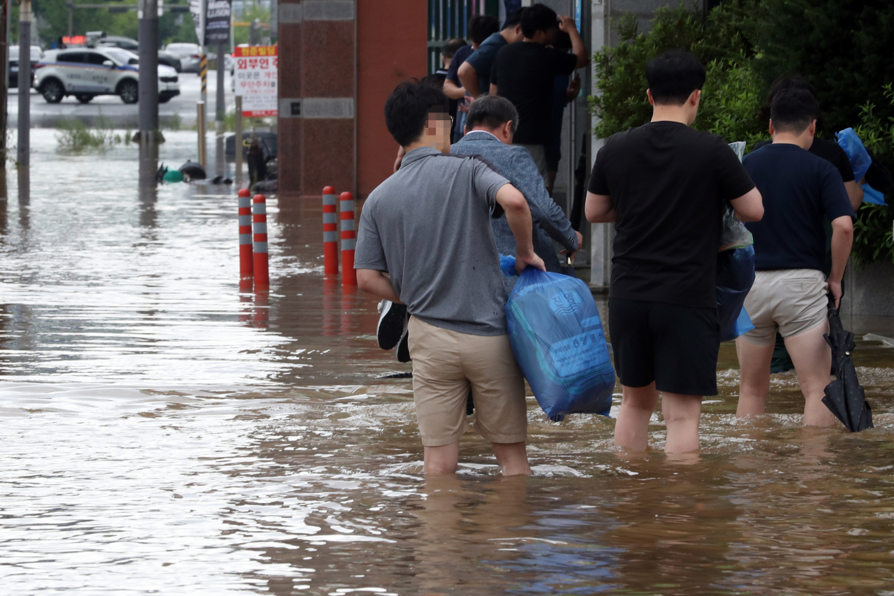 Workers commute through streets flooded by heavy rain in downtown Seokhyun-dong, Mokpo, South Jeolla Province on Monday morning.