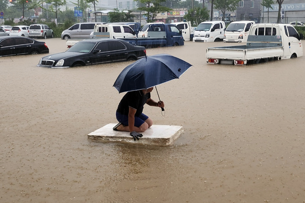A man climbs on a piece of insulation foam to travel across floodwaters at a used car dealership in Seokhyun-dong, Mokpo, South Jeolla Province, which was flooded by heavy overnight rains Monday. (Yonhap)