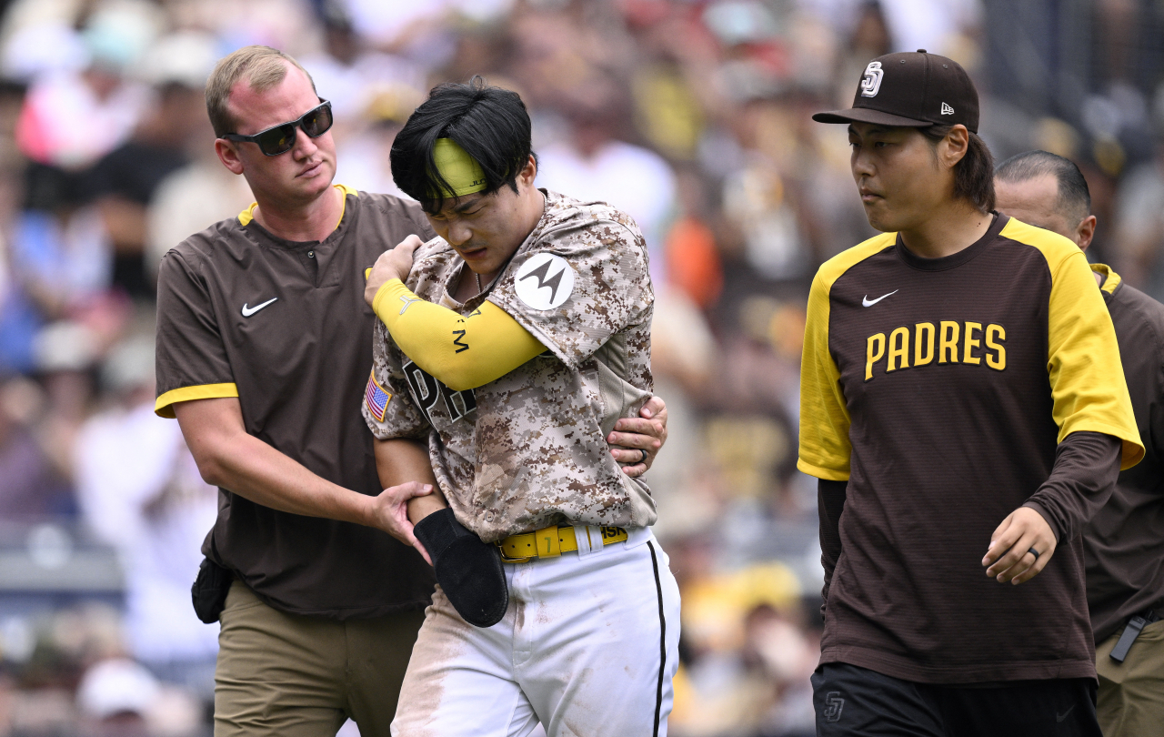 Kim Ha-seong of the San Diego Padres (center) is helped off the field by a team trainer after hurting his right shoulder on a slide home during the bottom of the third inning of a Major League Baseball regular season game against the Texas Rangers at Petco Park in San Diego on Sunday. (Reuters)