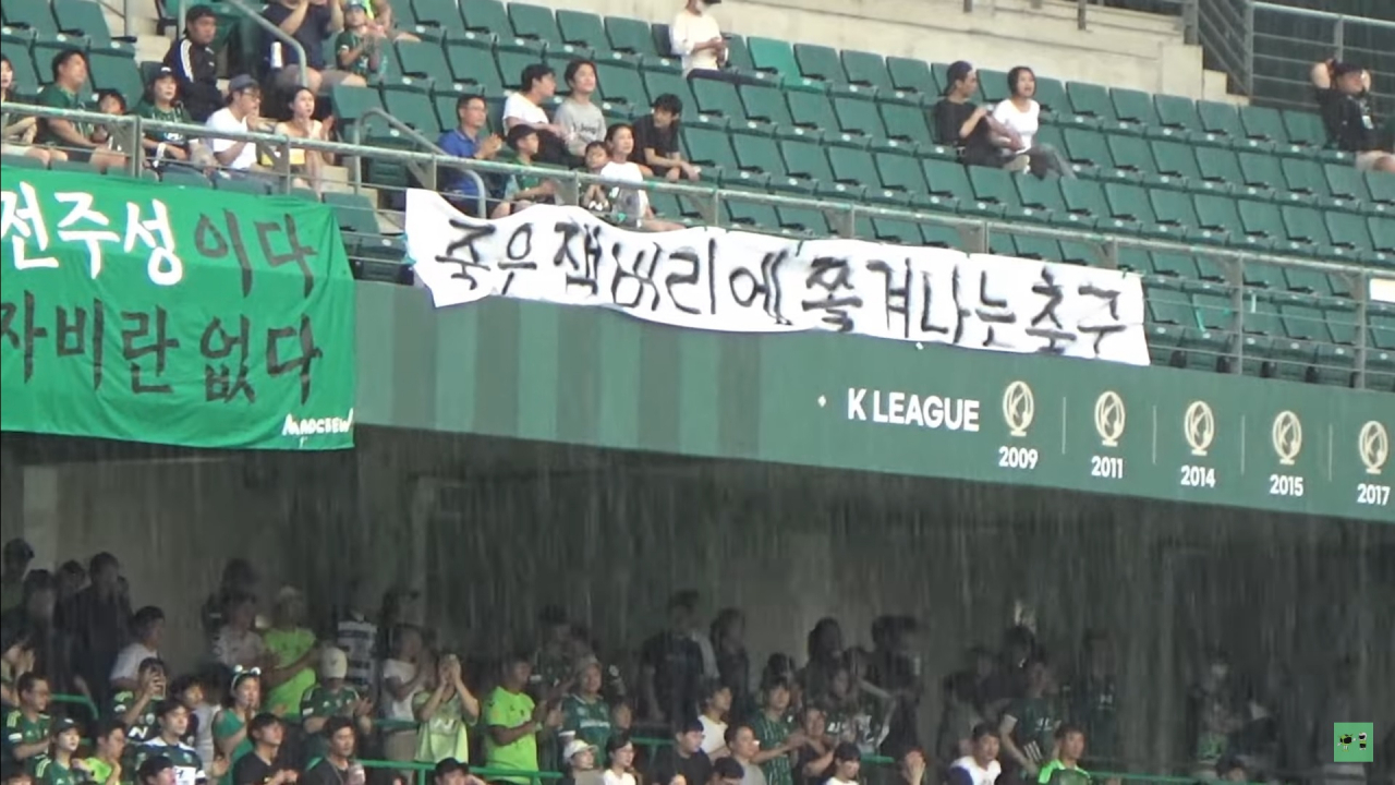 A screenshot image shows Jeonbuk Hyundai Motors FC fans hold a banner that reads 