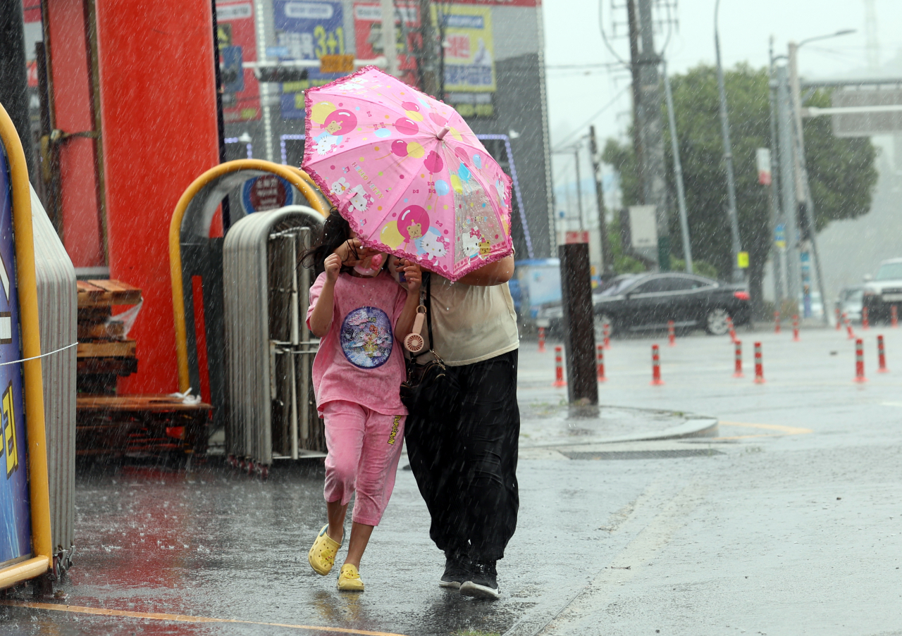 A woman and a girl share an umbrella while walking on a road in Yeosu, South Jeolla Province, on Thursday. (Yonhap)