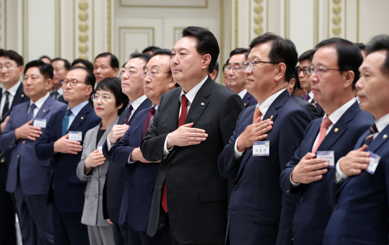 President Yoon Suk Yeol (front row, fourth from right) and other participants salute the national flag during a meeting of new members of the presidential Peaceful Unification Advisory Council at the former presidential office, Cheong Wa Dae, in Seoul on Tuesday. (Yonhap)
