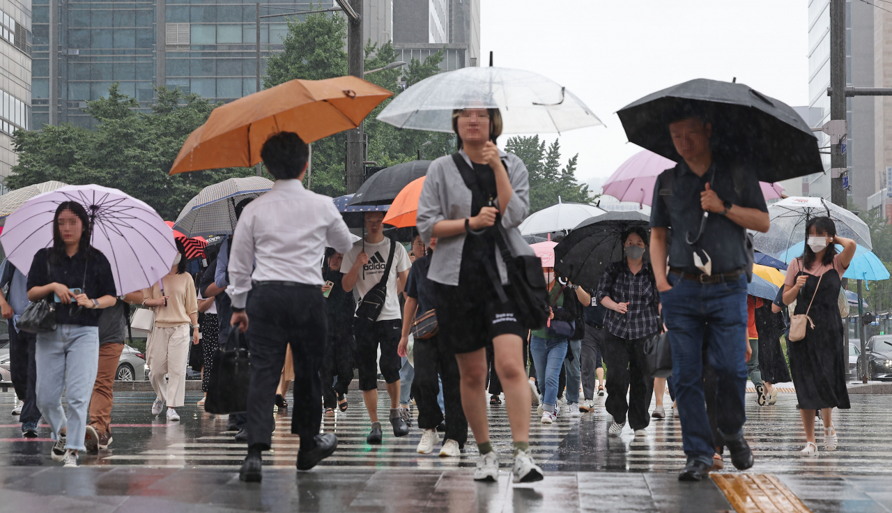People walk across a crosswalk near Gwanghwamun Square, Seoul, on Aug. 11, while the country was under the influence of Typhoon Khanun. (Yonhap)