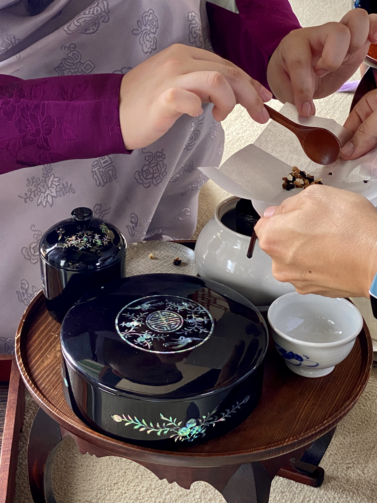 A guide dressed in traditional hanbok aids a visitor in putting herbs and nuts into a ceramic teapot. (Hwang Joo-young/The Korea Herald)