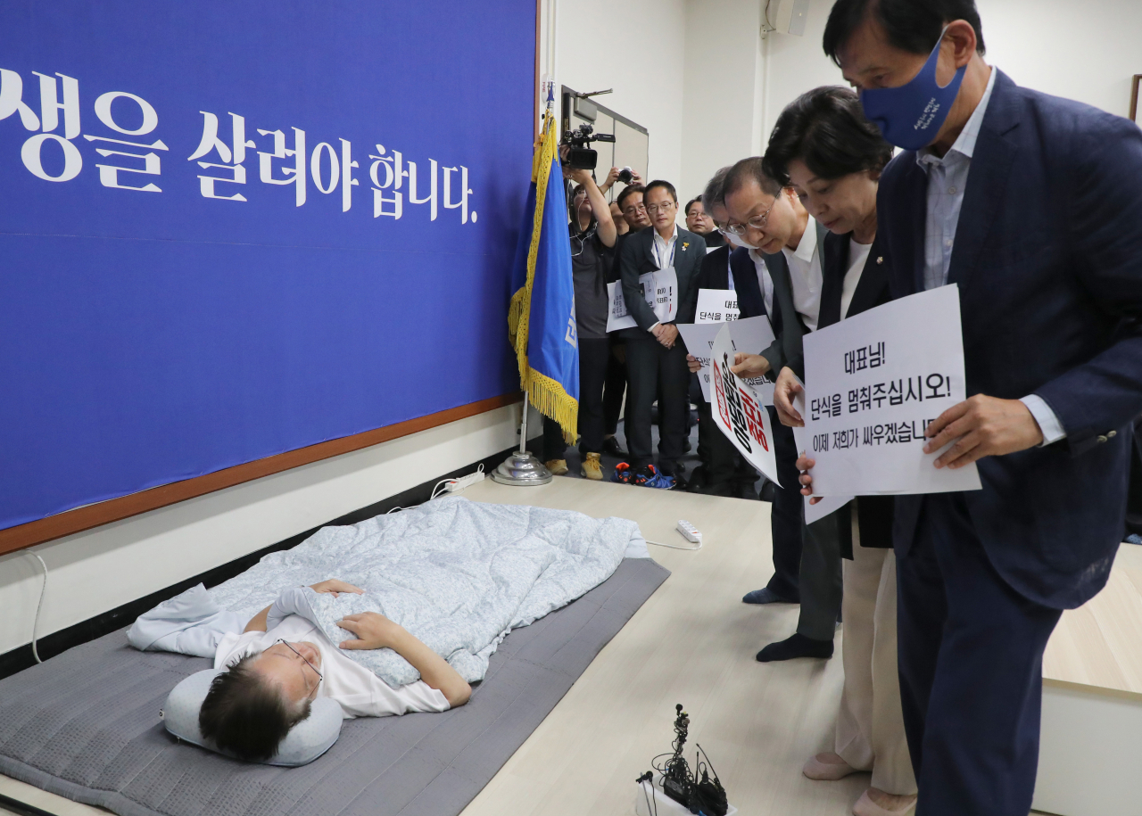 Democratic Party of Korea chair Rep. Lee Jae-myung, seen lying on the floor in white, is surrounded by fellow party lawmakers who are urging him to end his hunger strike on Saturday. (Yonhap)