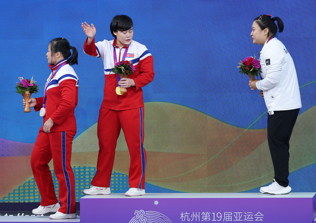 North Korean weightlifters Jong Chun-hui (L) and Song Kuk-hyang (C) leave the victory ceremony for the women's 76kg weightlifting event at the Asian Games, with Kim Su-hyeon of South Korea behind them on the podium at Xiaoshan Sports Centre Gymnasium in Hangzhou, China, on Thursday. (Yonhap)