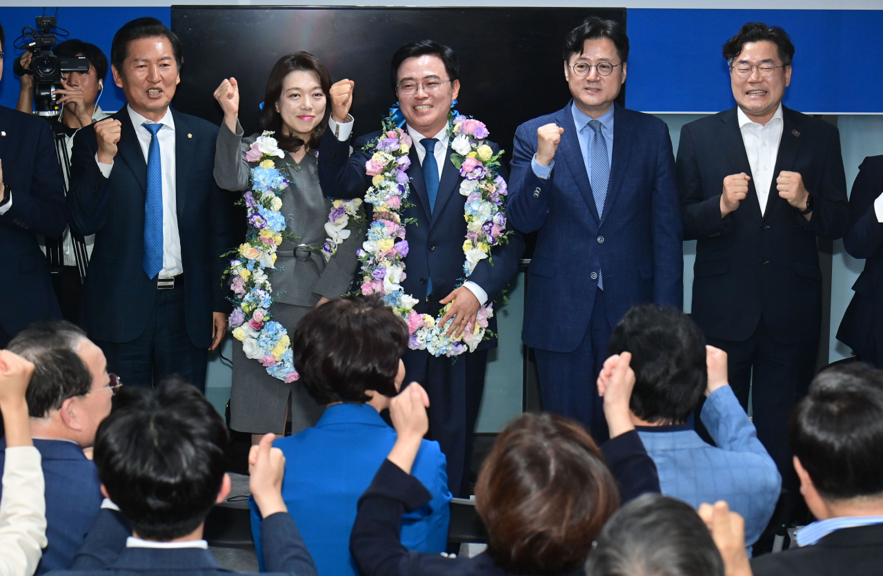Jin Kyo-hoon, the main opposition Democratic Party's candidate in the by-election for the new chief of Seoul's Gangseo Ward, and other party officials cheer as they watch television screens broadcasting the provisional results at his campaign office on Wednesday night. (Yonhap)