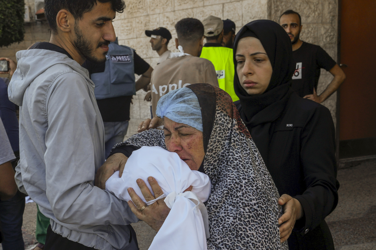 A Palestinian woman kisses the sheet-covered body of a child killed during an Israeli airstrike, Sunday, outside al-Aqsa Hospital in Deir el-Balah, central Gaza Strip. (AP-Yonhap)