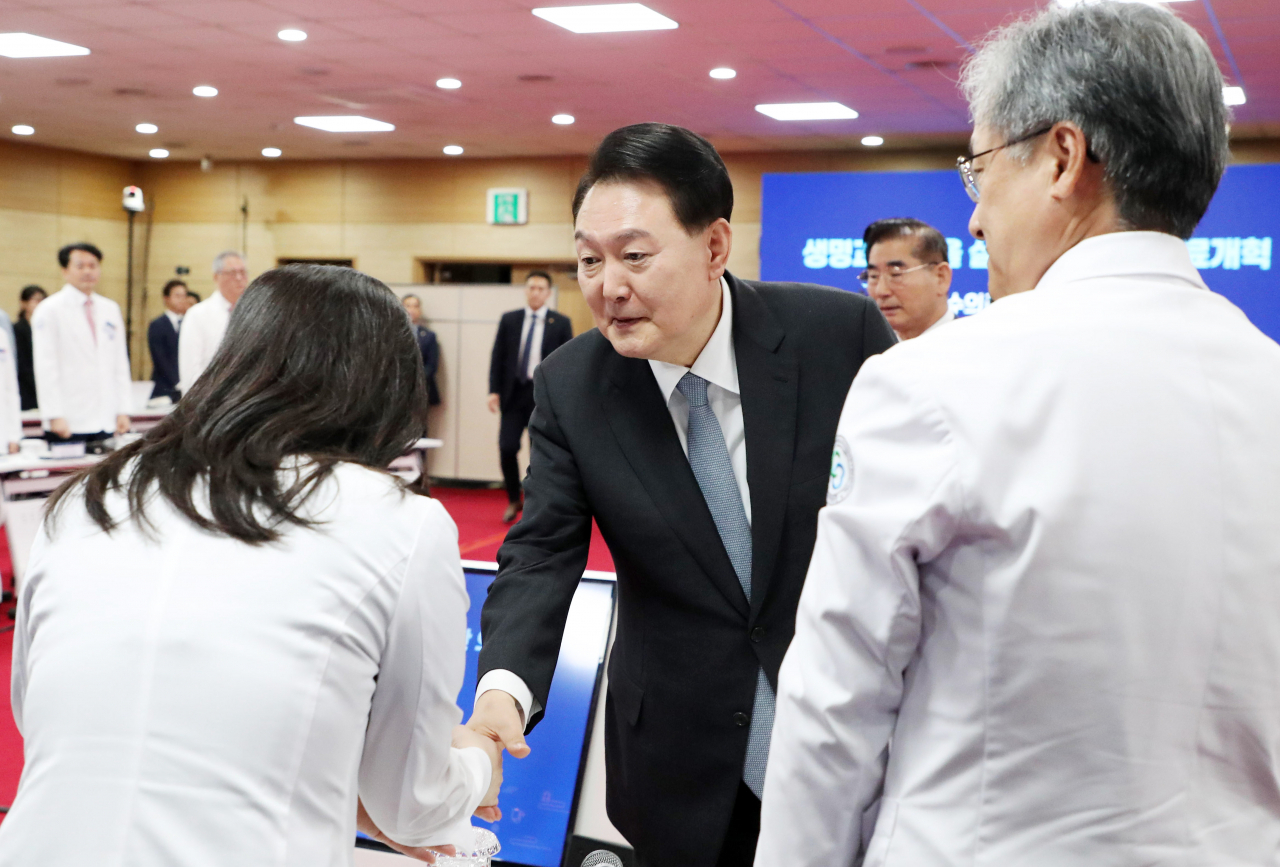 President Yoon Suk Yeol shakes hand with doctors who attended a meeting with ministers, lawmakers and medical experts at Chungbuk National University on Thursday. (Yonhap)