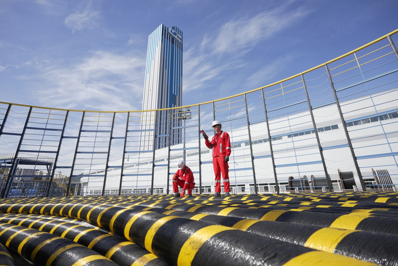 At the Donghae plant in Gangwon Province, engineers from LS Cable & System inspect cables wound on a cable drum, with Asia's largest 172m-tall vertical cable processing tower, standing in the background. (LS Cable & System)