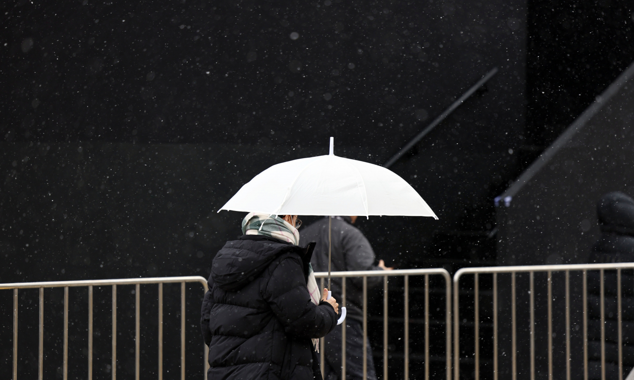 A passerby walks through Gwanghwamun Square, central Seoul, holding an umbrella as the first snow fell, Friday. (Yonhap)