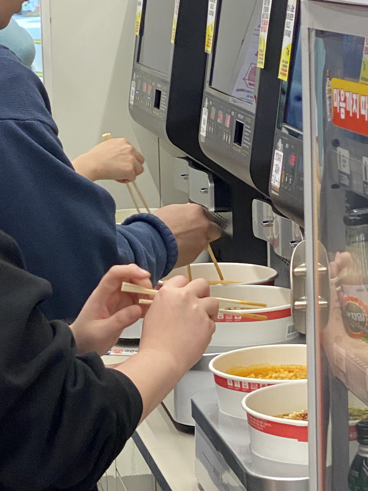 Customers cook noodles on a special machine at CU's Hongdaesangsang branch in Mapo-gu, Seoul, Thursday. (Hwang Joo-young/The Korea Herald)
