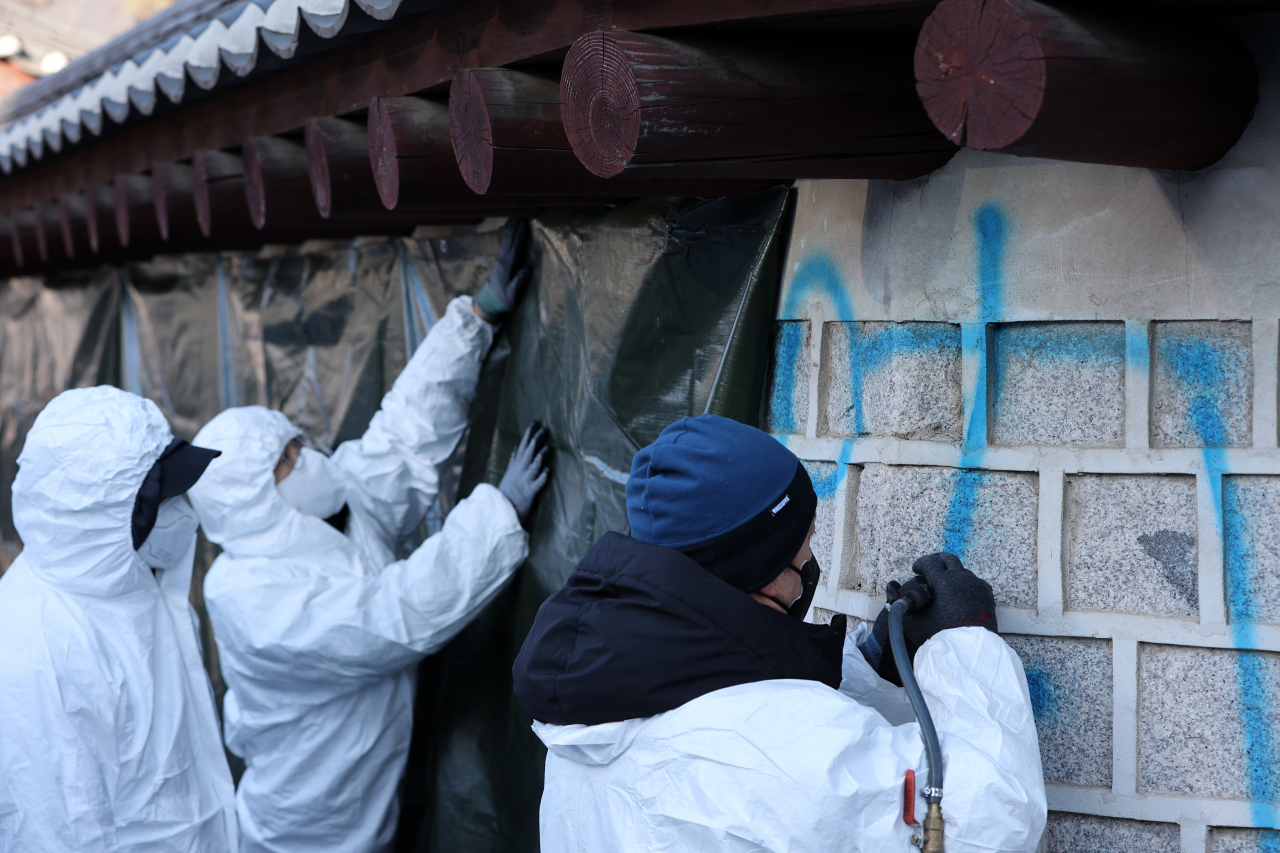 Officials from the National Research Institute of Cultural Heritage tries to wipe off the graffiti on the wall of the Gyeongbok Palace in central Seoul on Sunday. (Yonhap)