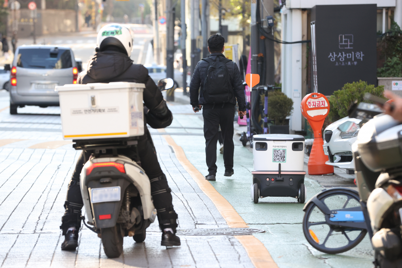 This photo shows a deliveryman on a motorcycle and an unmanned delivery robot, which in South Korea serve as a backbone of South Korea's e-commerce ecosystem. (Yonhap)