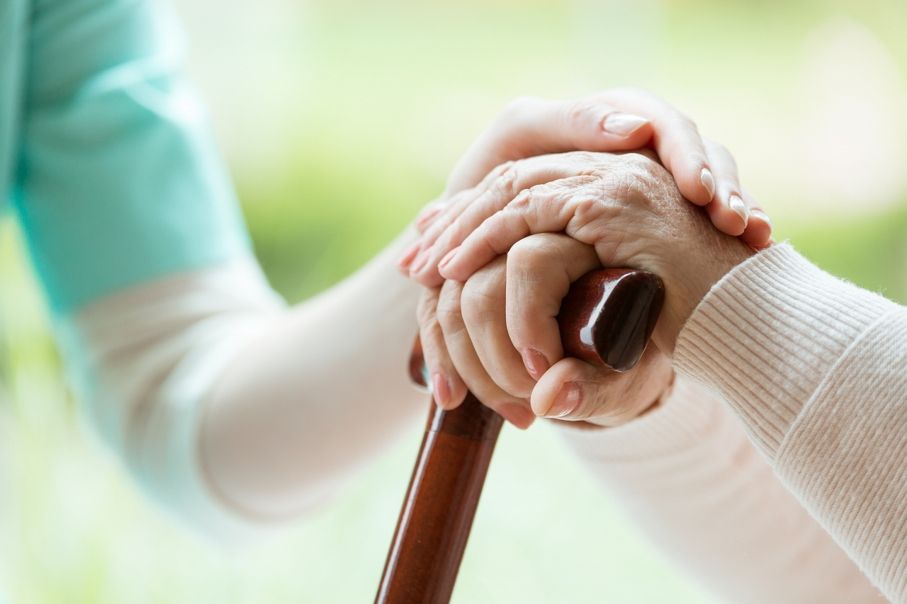 A caregiver has a hand over an old person's hand holding a cane. (123rf)