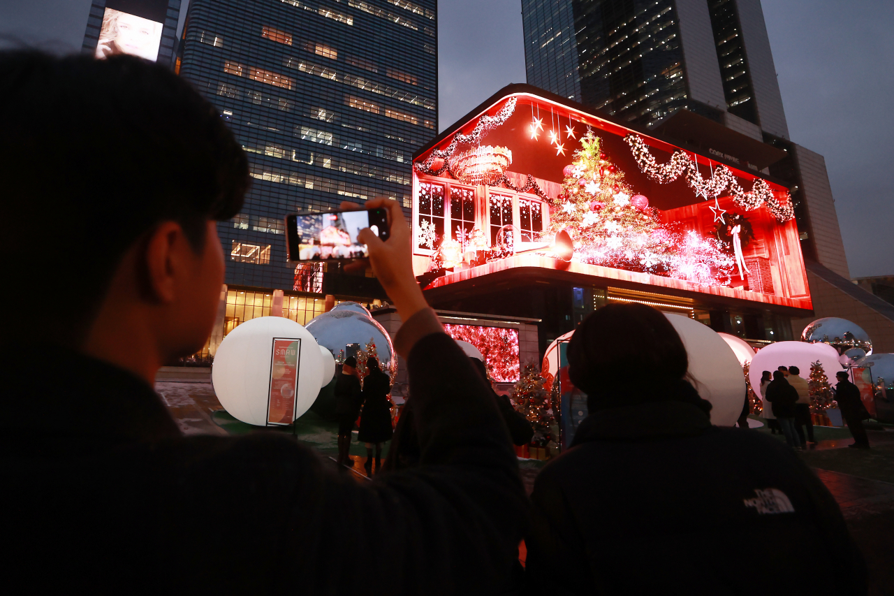 People enjoy the 'Christmas Media Show' in front of a large electronic board at COEX K-Pop Square in Gangnam, Seoul, as part of its 2023 Seoul Media Art Week. Gangnam district hosts special Christmas-themed media shows on 71 electronic boards around the trade center until Dec. 25. (Yonhap)