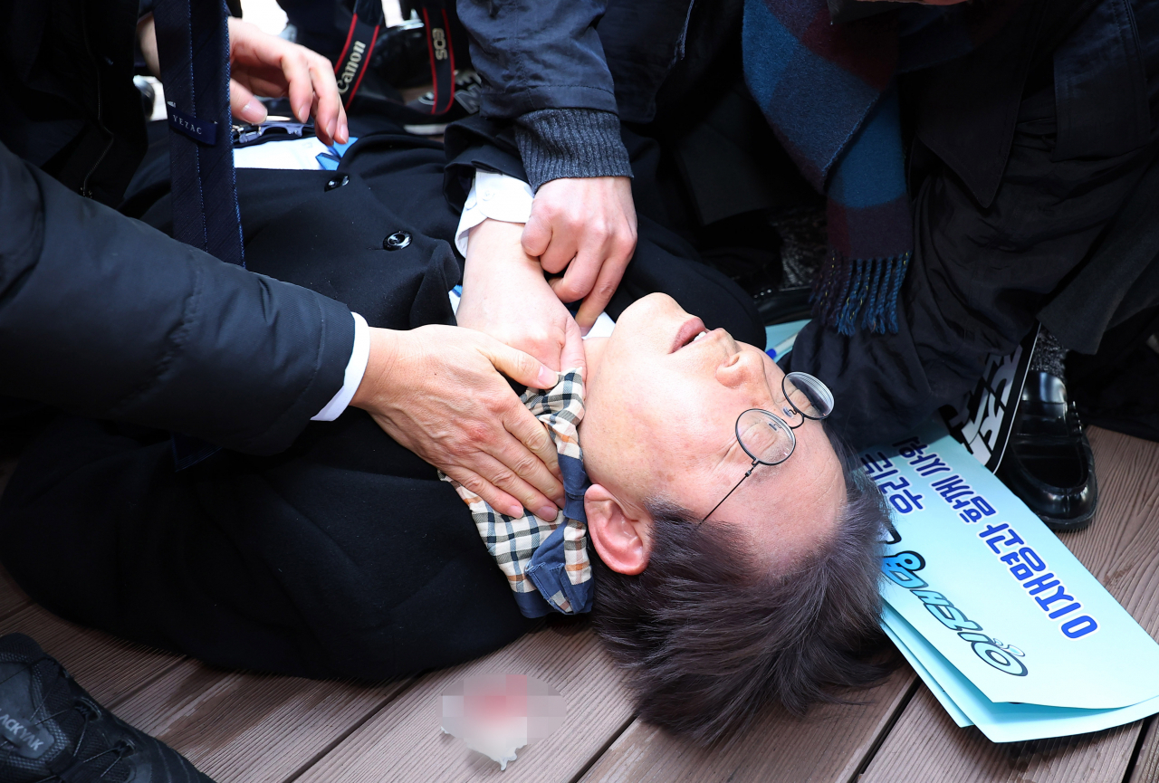 Lee Jae-myung, leader of the main opposition Democratic Party of Korea, lies on the ground after being stabbed in the left side of his neck during a visit to the construction site of an airport on Gadeok Island off Busan on Tuesday. (Yonhap)