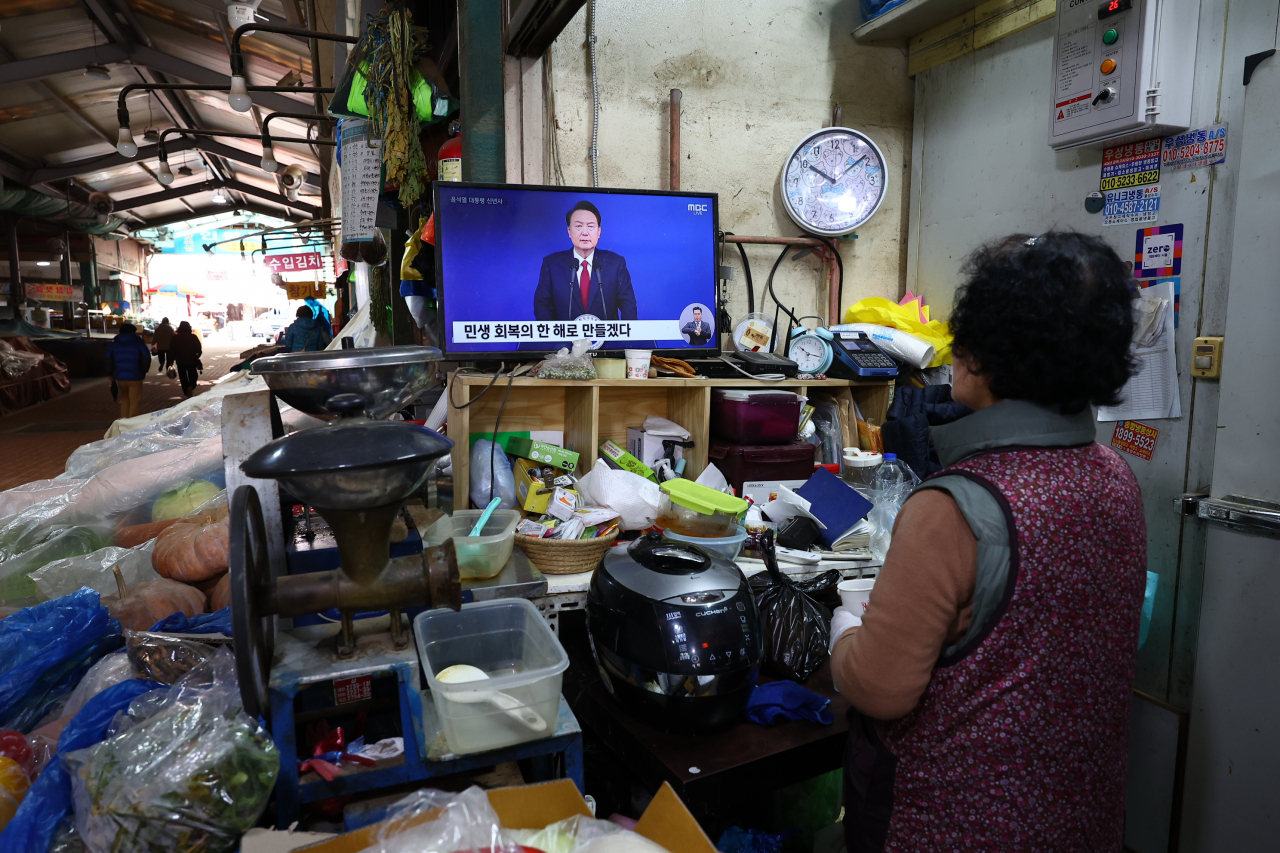 A vendor in a traditional market in Seoul watches President Yoon Suk Yeol's televised address to the nation on Jan. 1. (Yonhap)