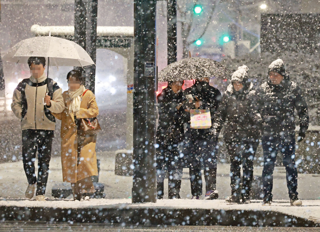 Pedestrians wait to cross the street as snow falls near Anguk Station in Seoul, Saturday. (Yonhap)