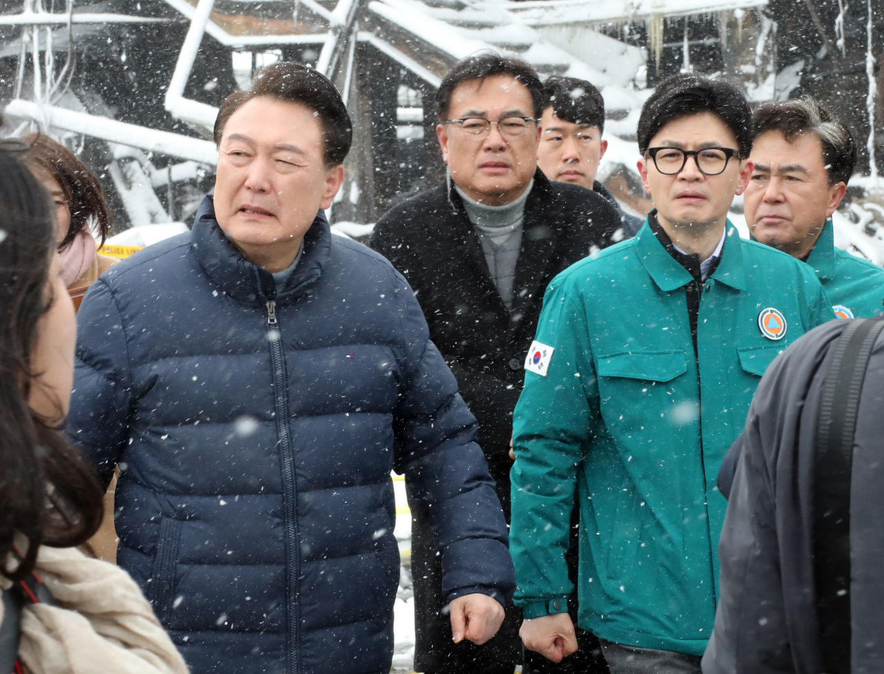 President Yoon Suk Yeol (left, front row) and People Power Party's interim leader Han Dong-hoon (right, front row) walk together on Tuesday afternoon at a traditional market in Seocheon, South Chungcheong Province, as they inspected the site of a fire that damaged over 200 stores Monday night. (Yonhap)