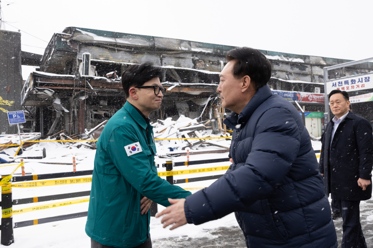 President Yoon Suk Yeol (right) and People Power Party's interim leader Han Dong-hoon shake hands on Tuesday afternoon at a traditional market in Seocheon, South Chungcheong Province, as they inspected the site of a fire that damaged over 200 stores Monday night. (Presidential Office)