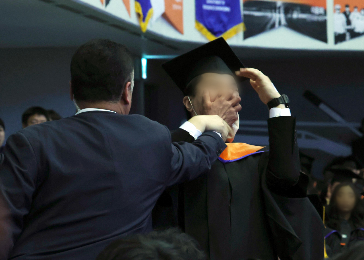 A man identified as Shin Min-gi (right), a student graduating from KAIST, is seen being deterred by a presidential bodyguard after he protested the government's 2024 scientific research-related budget cut by 15 percent during President Yoon Suk Yeol's commencement speech at the university in Daejeon on Friday. (Yonhap)