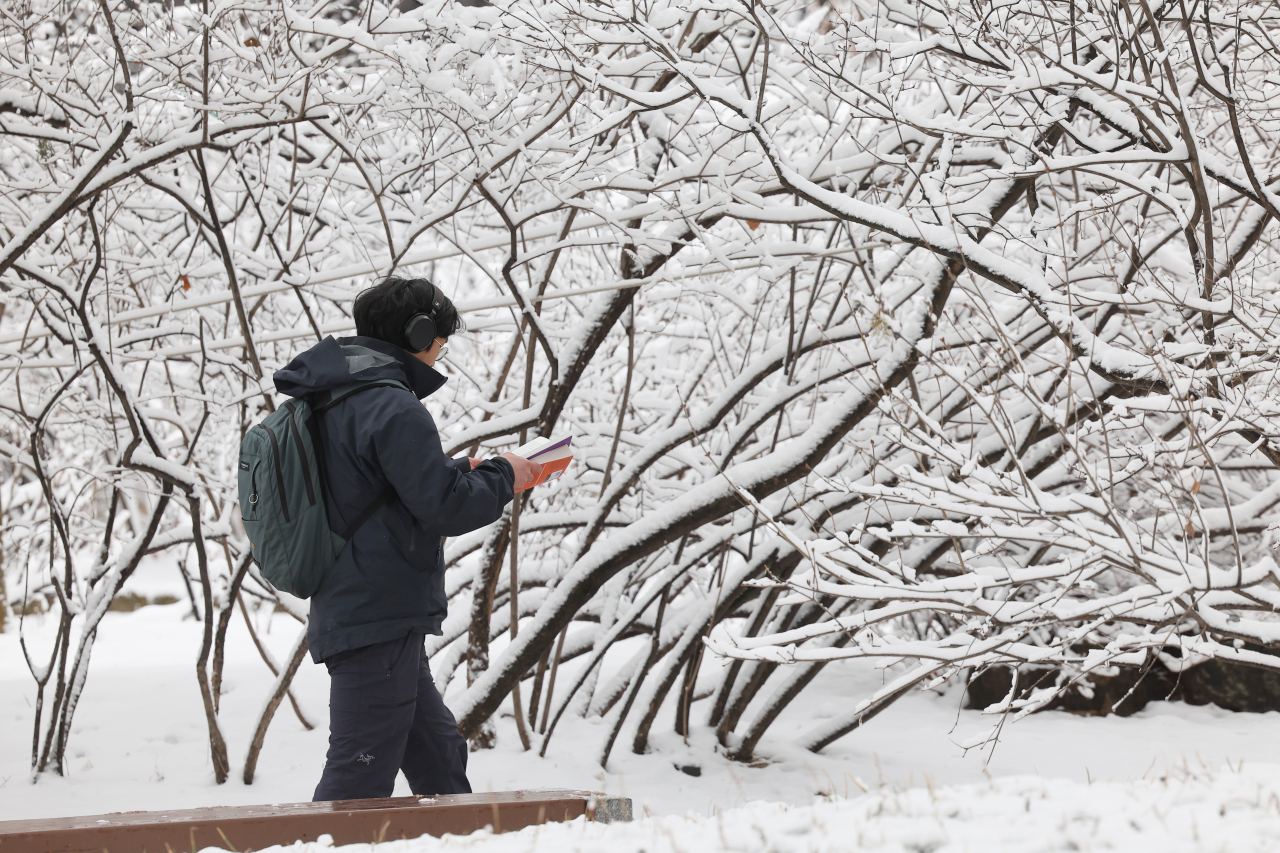 A passerby walks by while reading a book near Deoksugung in Jung-gu, central Seoul, Thursday. (Yonhap)