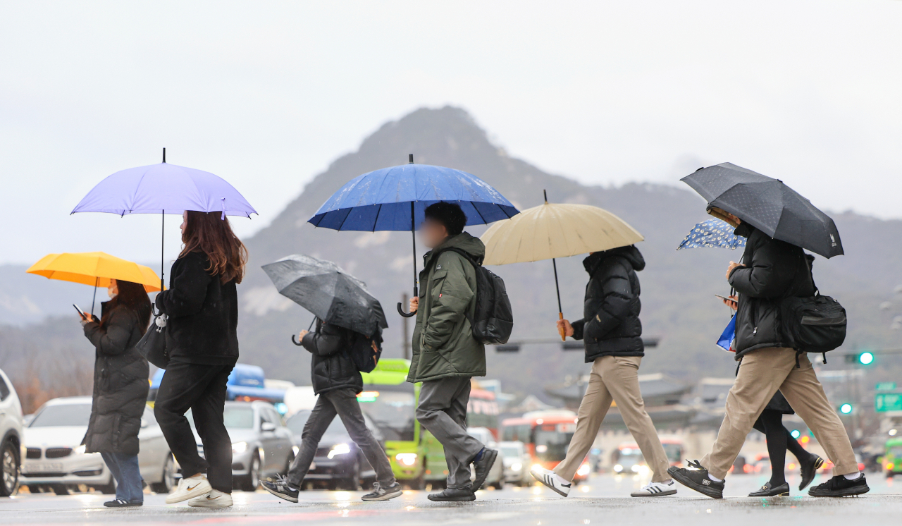 Passersby walk on a crosswalk while holding umbrellas near Gwanghwamun Square in Seoul on Feb. 21. (Yonhap)