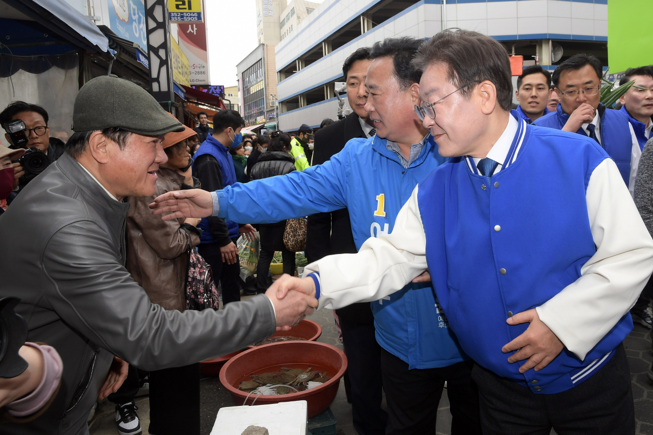 Democratic Party of Korea Chair Lee Jae-myung (right) shakes hands with a traditional market vendor while visiting Dangjin, South Chungcheong Province, Friday, (Pool photo via Yonhap)