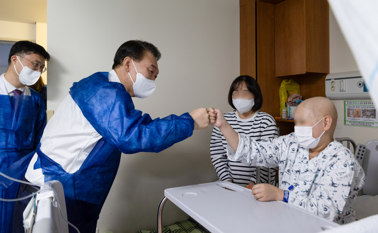 President Yoon Suk Yeol (second from left) fist-bumps a young cancer patient during a visit to Asan Medical Center in Seoul on March 18, amid a nearly monthlong walkout by more than 11,000 trainee doctors protesting the government's plan to increase medical student enrollment. (The Presidential Office)