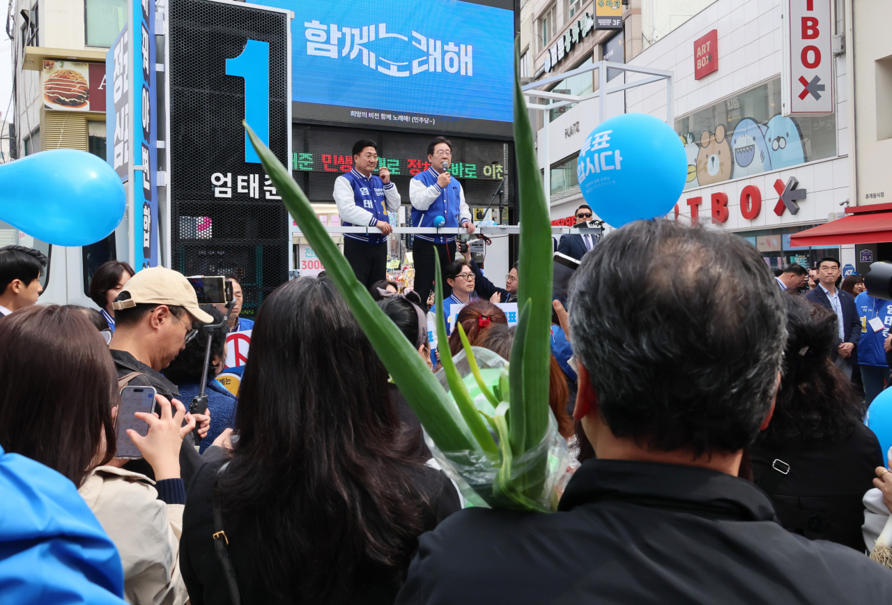 A citizen holds a bundle of green onions as Democratic Party of Korea Chair Rep. Lee Jae-myung (right, on stage) delivers his speech during his visit to Icheon, Gyeonggi Province, on Saturday. (Yonhap)
