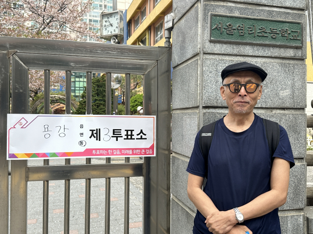 Han Suk-lim, 65, poses next to a polling station notice at Yeomri Elementary School in Mapo-gu, western Seoul, Wednesday. (Lee Jung-joo/The Korea Herald)